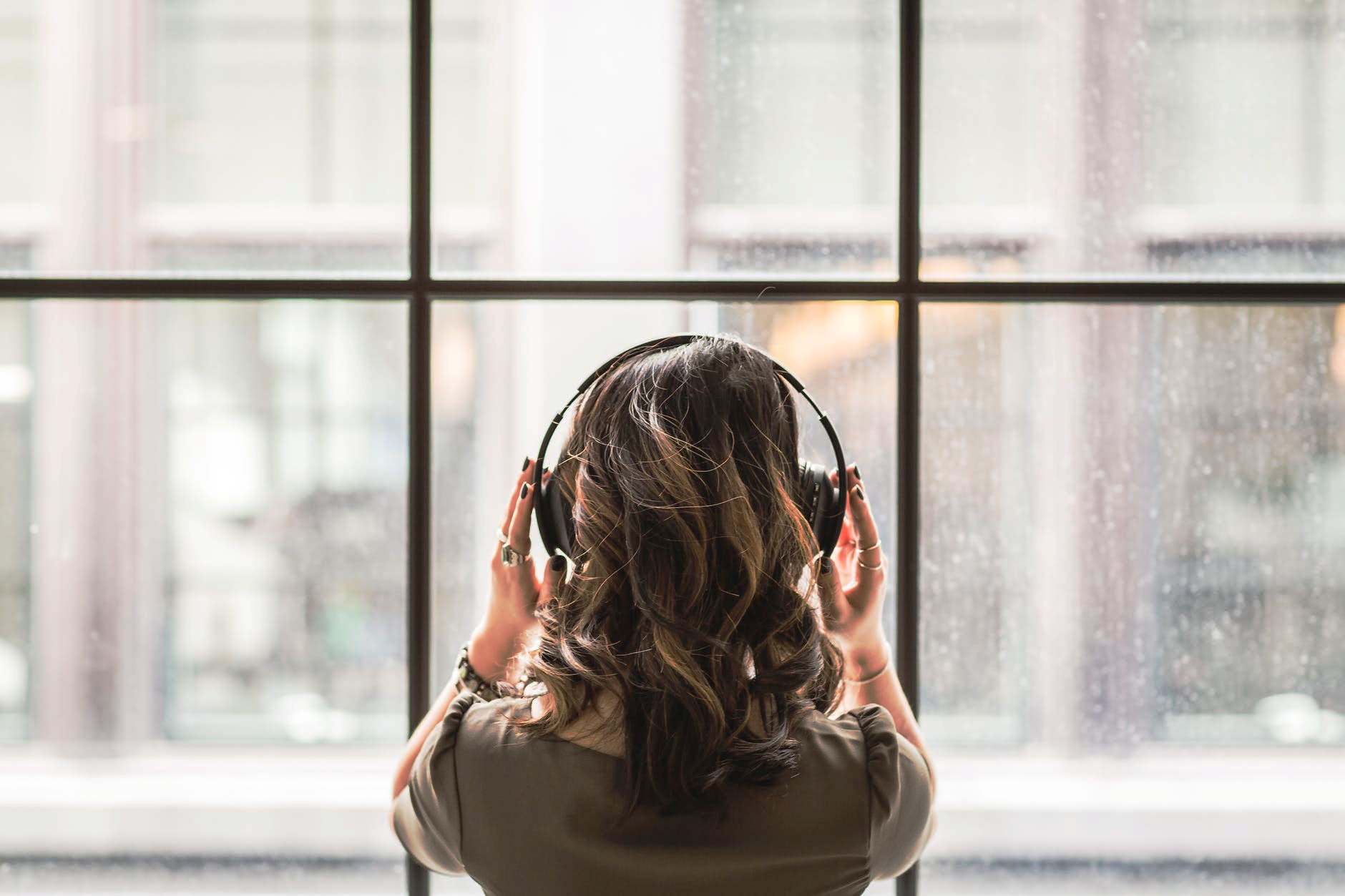 Kobieta patrząca w okno ze słuchawkami na uszach
